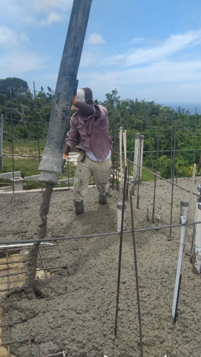 Worker directing concrete line pump on slab pour, Jamaica